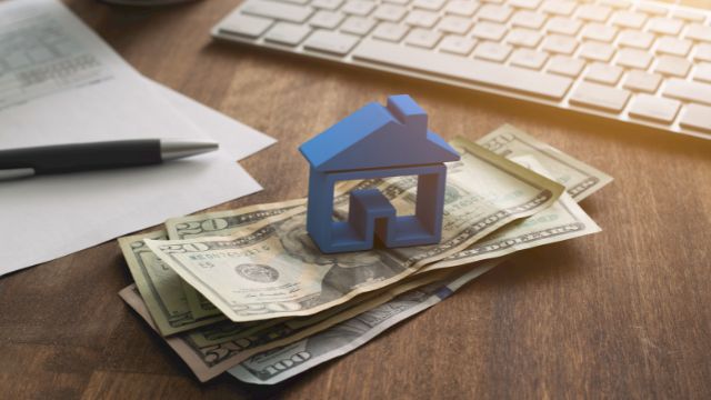 a%20blue%20home%20figurine%20resting%20on%20a%20money%20with%20a%20contract%20in%20the%20background